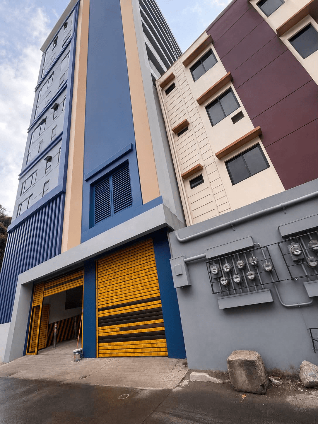 Street-level photograph looking up at Aleevia Carter Residences, showing its blue, cream, and burgundy facade above the building entrance.